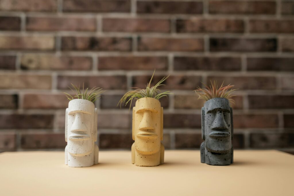 Colorful Moai head planters against a rustic brick wall, showcasing unique decor.